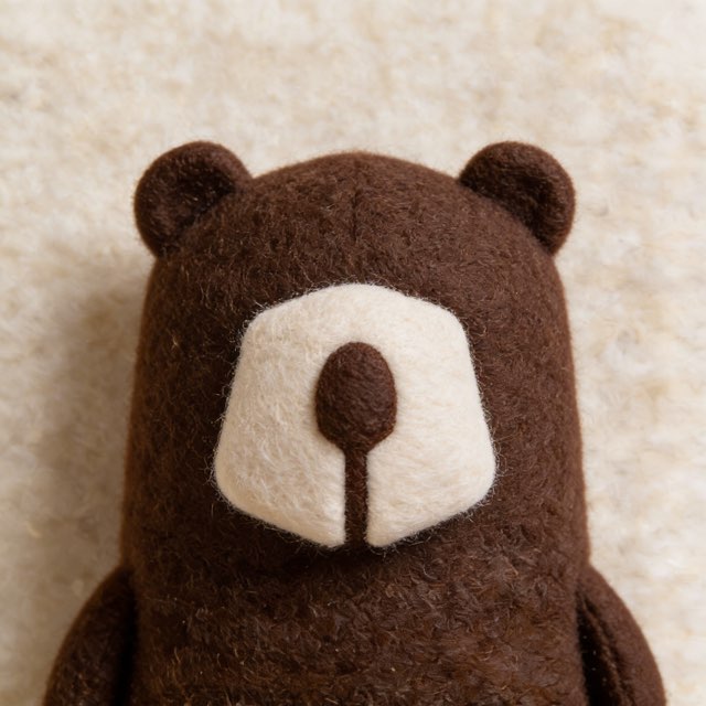 Generated for Kova. The Kova bear mark needle-felted as a soft plush figure, brown wool with a cream snout.